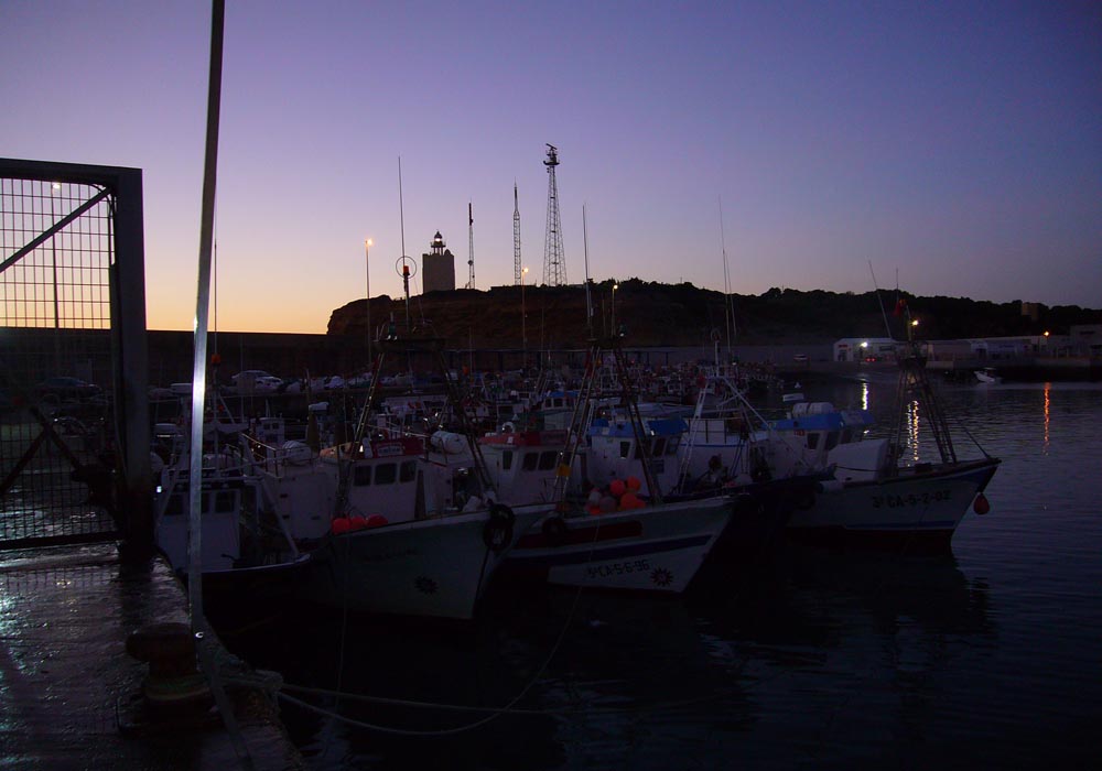 Vista del muelle pesquero y el faro al atardecer